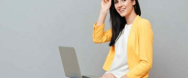 photo young pretty woman wearing eyeglasses dressed yellow jacket sitting stool while using laptop grey surface