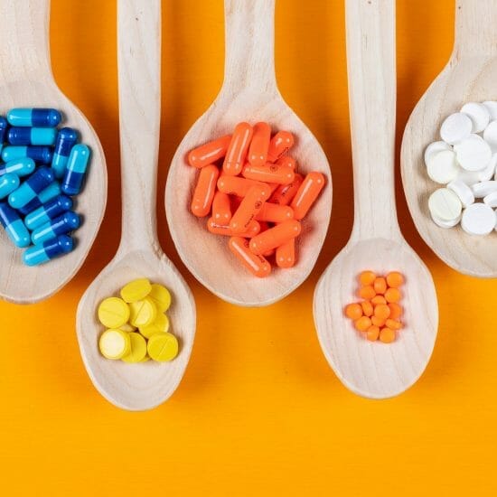 Top view colorful pills in wooden spoons on orange background. horizontal